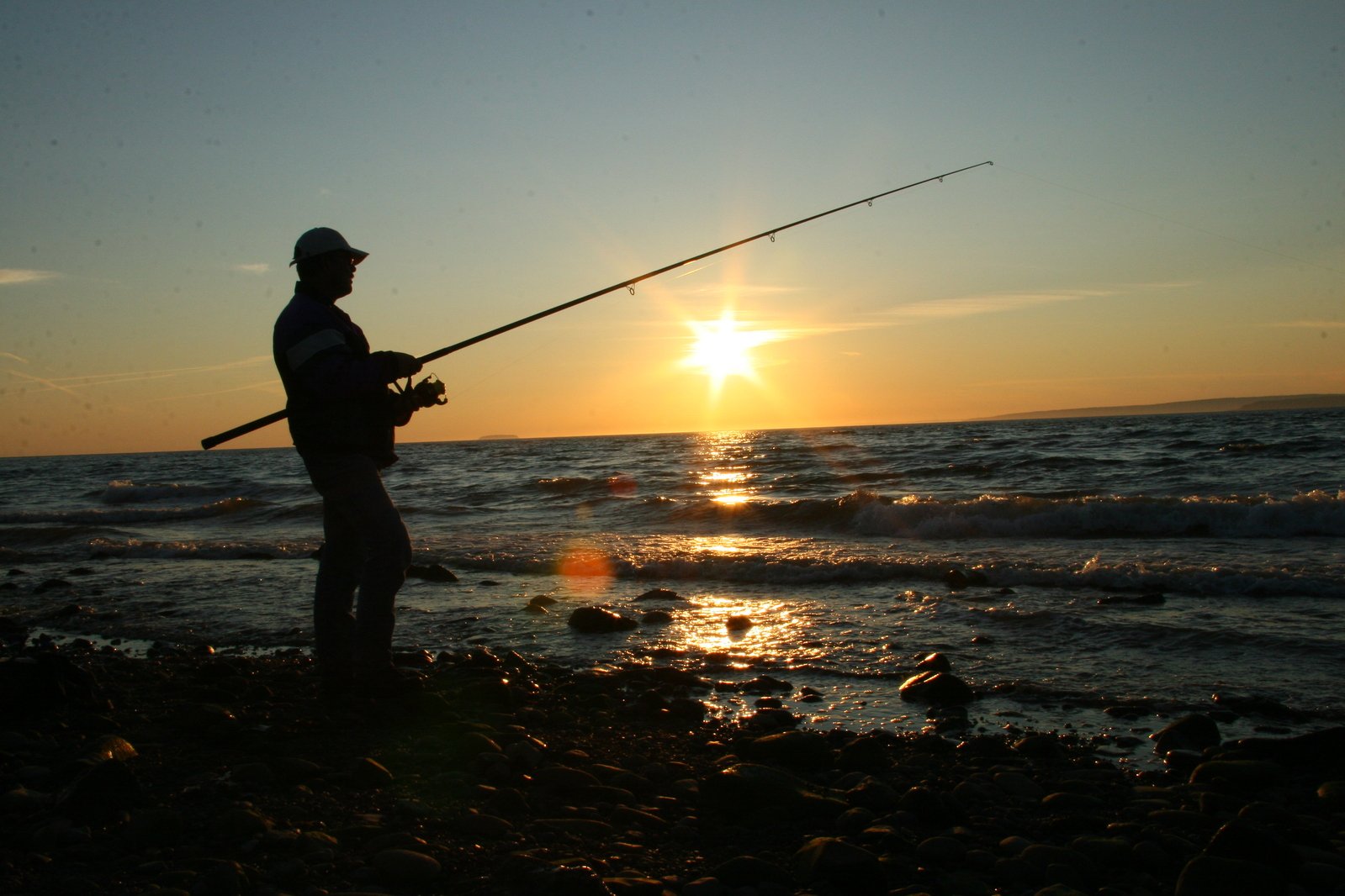 a man holding fishing poles standing in water with sun reflecting off of back