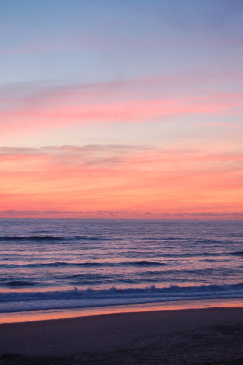 a sunset view looking back at a beach with a small ship in the distance