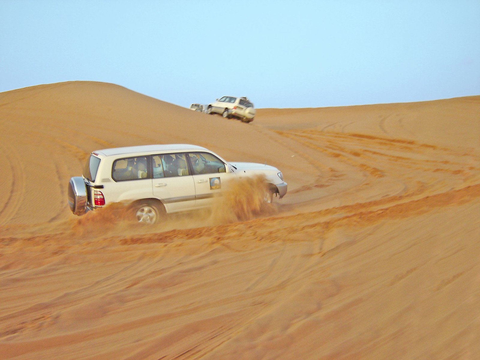 a car driving in the sand near several vehicles