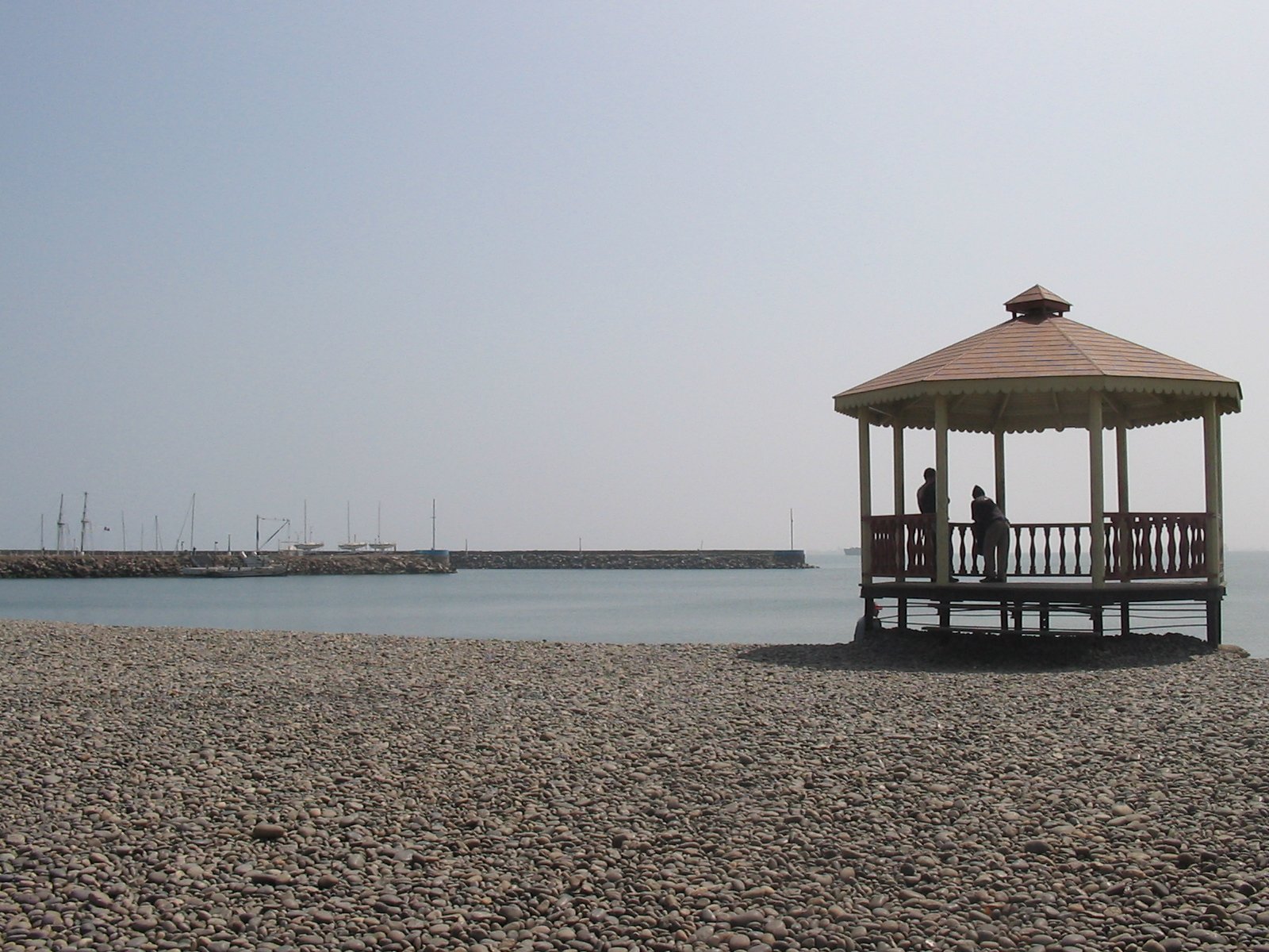 a man in a white shirt stands on a wooden pier with a wooden gazebo, on the shore