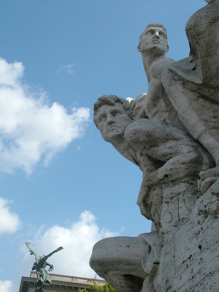 a statue stands between two large statues on the side of a wall