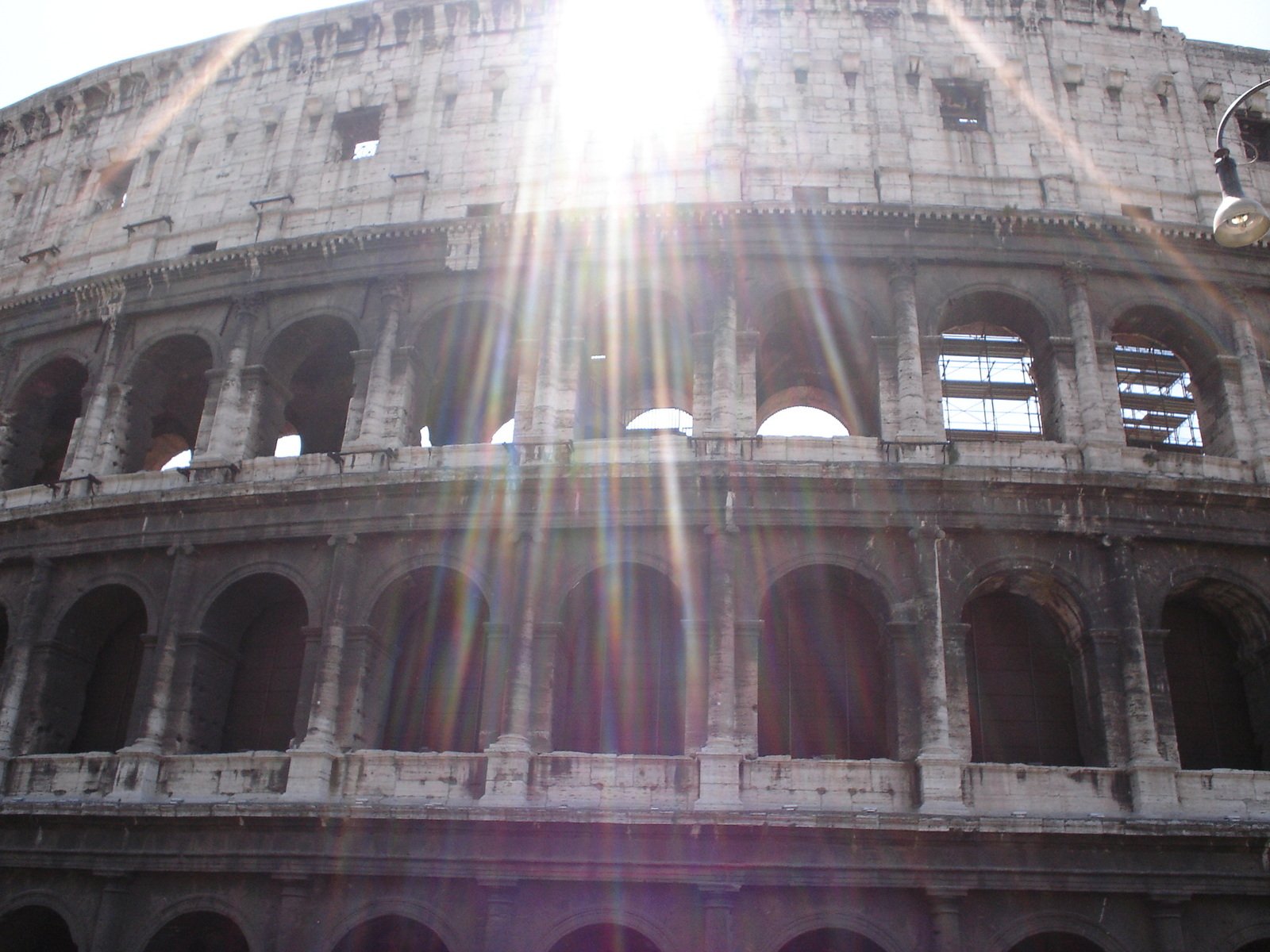 sun shining through arch of the colossion in rome