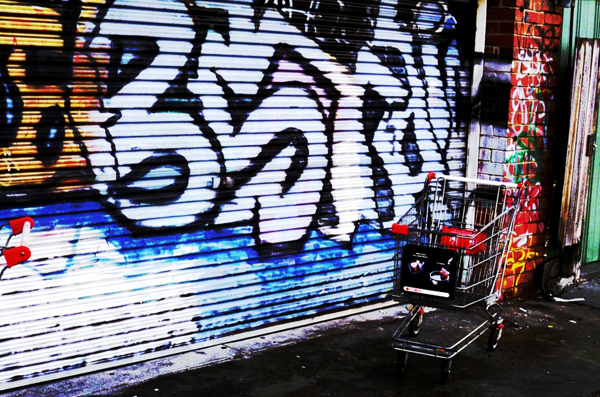 a graffiti covered wall has a shopping cart parked near it