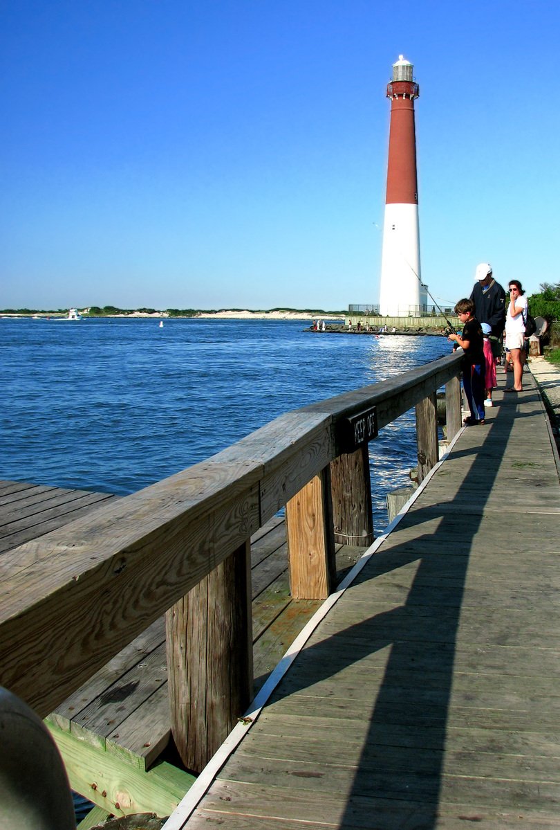 people walking on a walkway towards a lighthouse by water