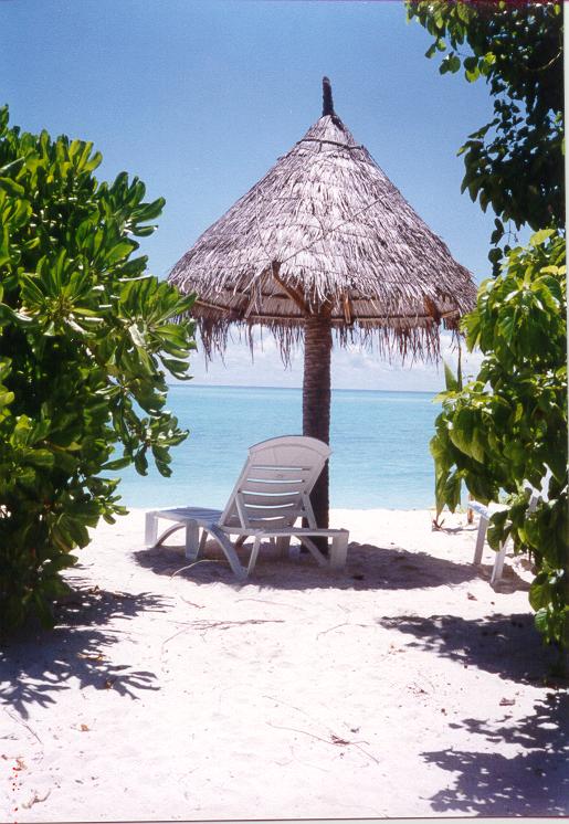 the white sand beach is covered with a straw roof and lounge chairs