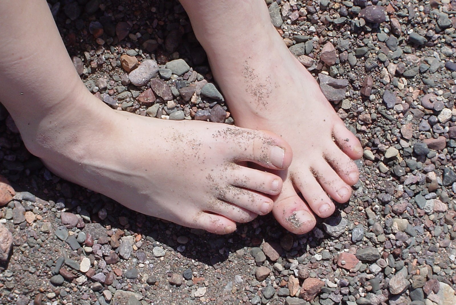 two bare feet on the ground with small rocks
