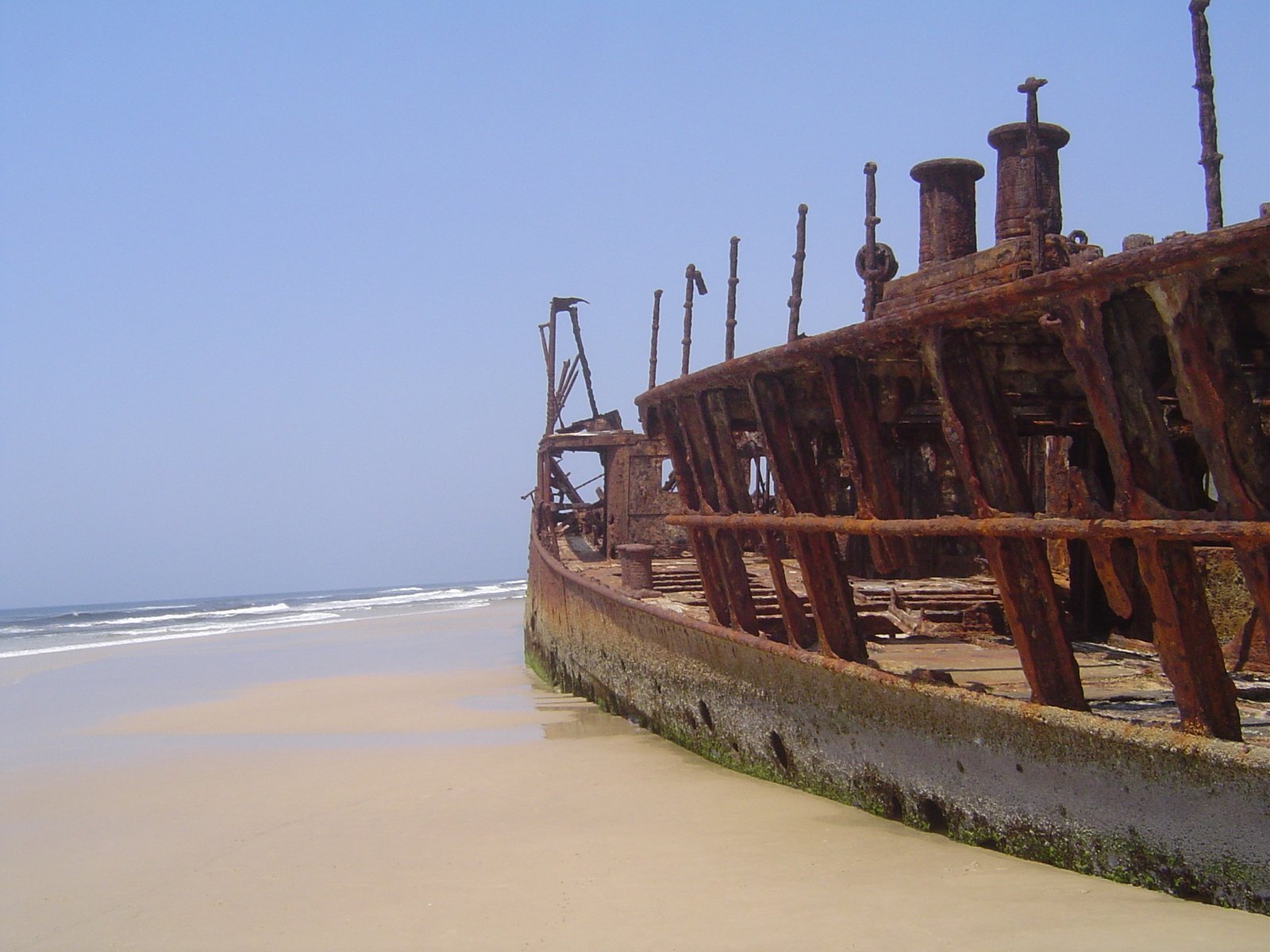 a very old ship sitting in the sand at the ocean