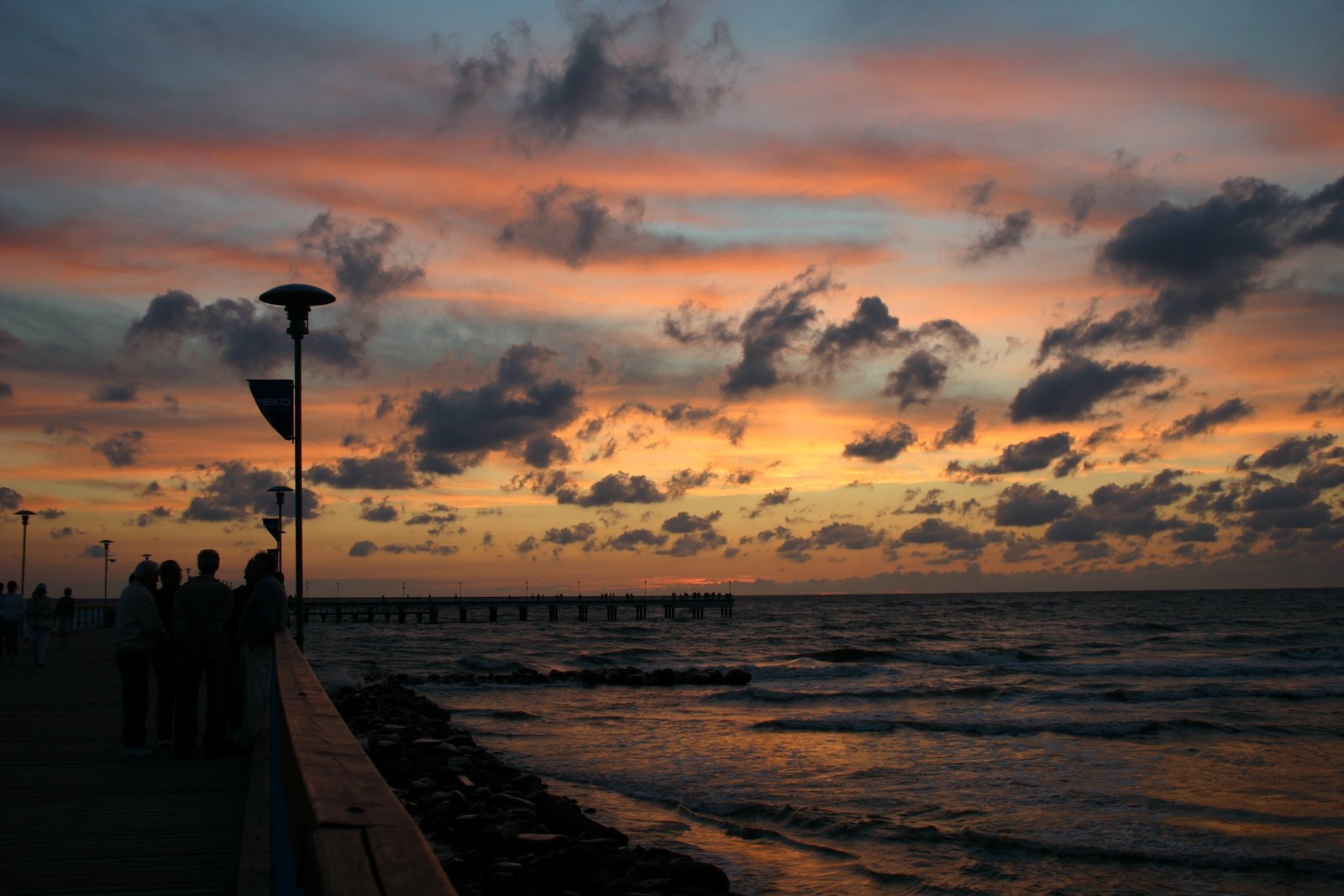 some people walking on a pier as the sun goes down