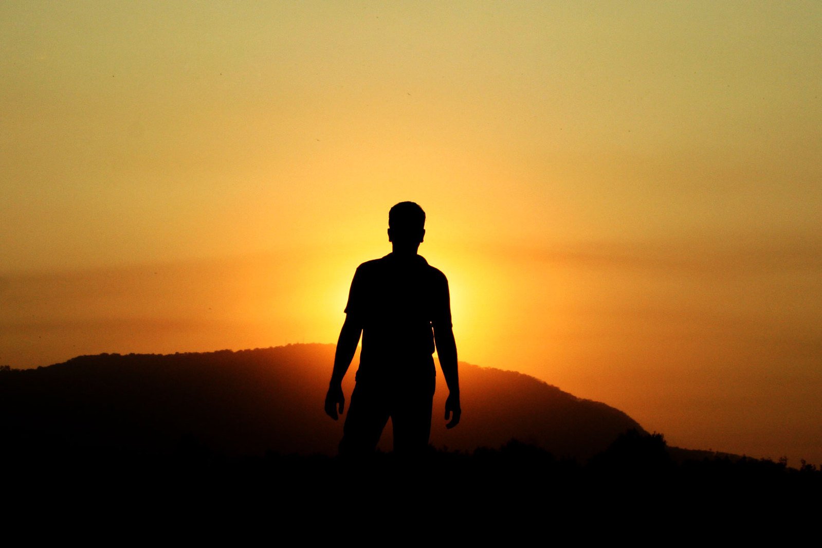 the silhouette of a man standing at sunset
