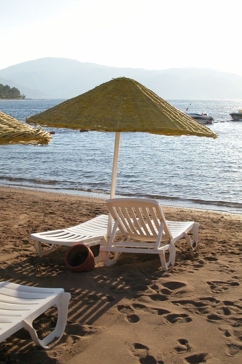 two lawn chairs sitting on a sandy beach near an umbrella