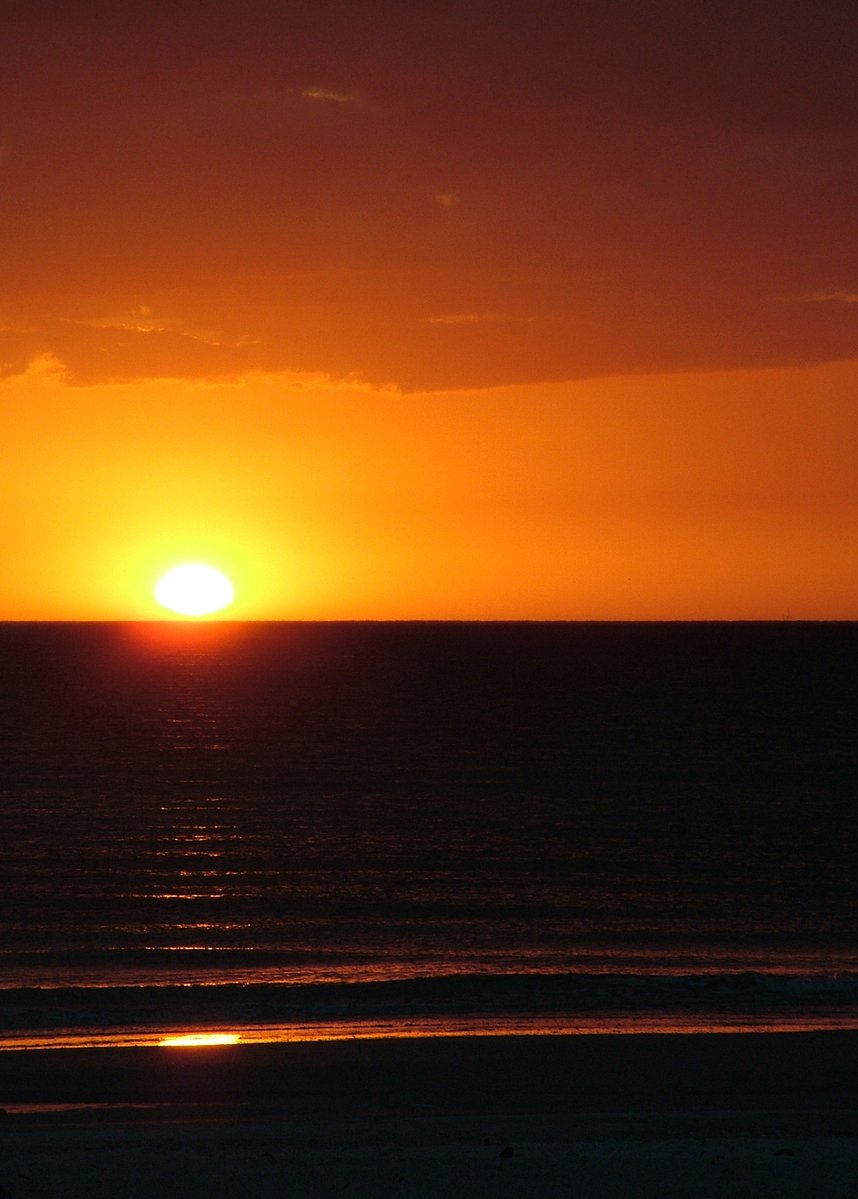 the sun is rising over the horizon on a beach