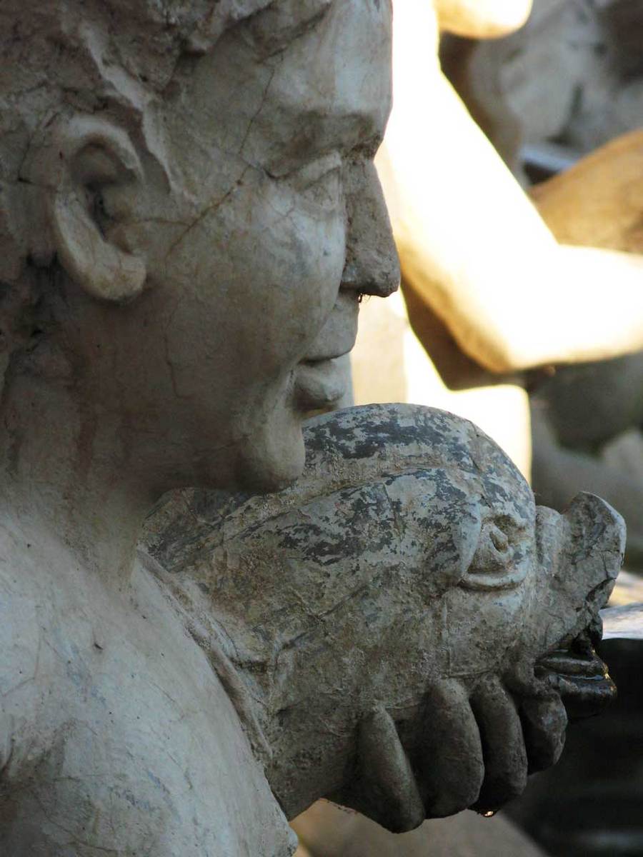 an older marble statue holding a rock and some rocks