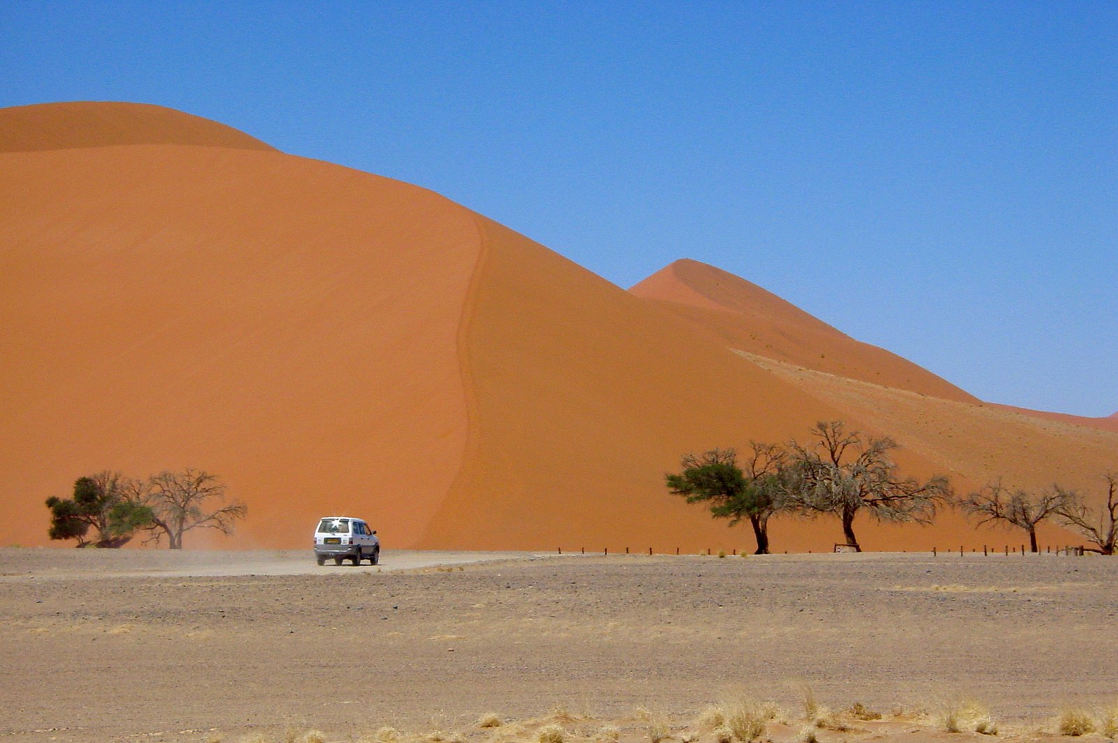 a jeep driving through the desert in front of large sand dunes