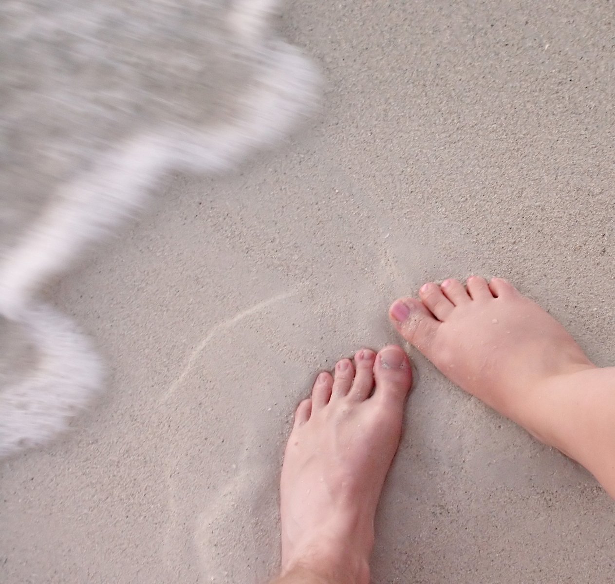 a persons feet sticking out of the sand near the water