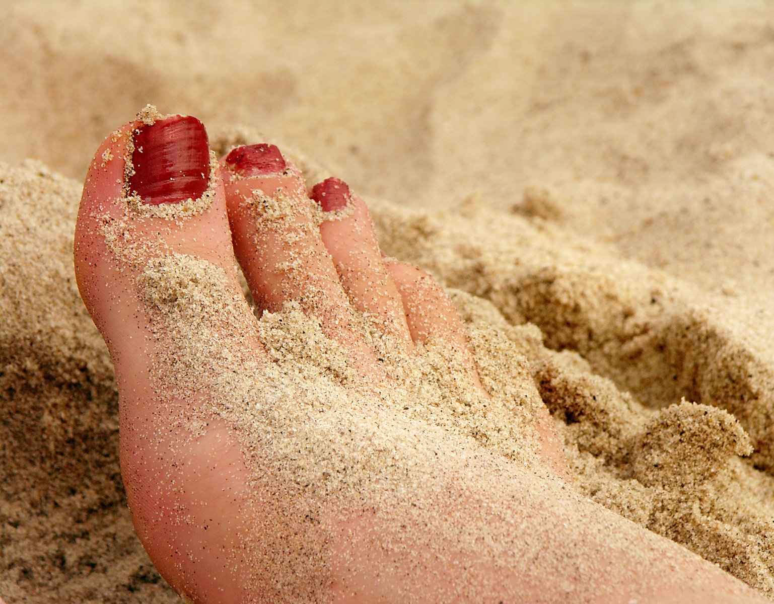 a person is standing on the sand with red nails
