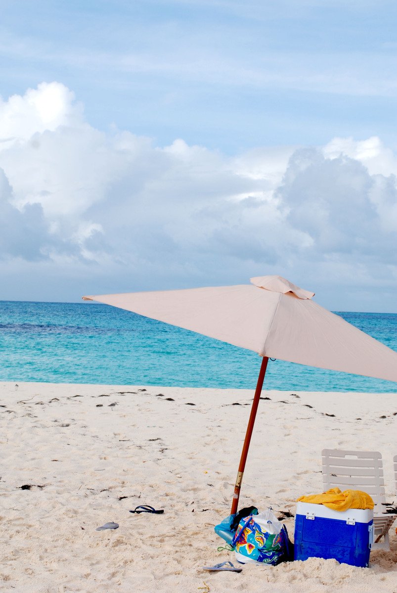 a picnic area on a beach with an umbrella, cooler, and basket