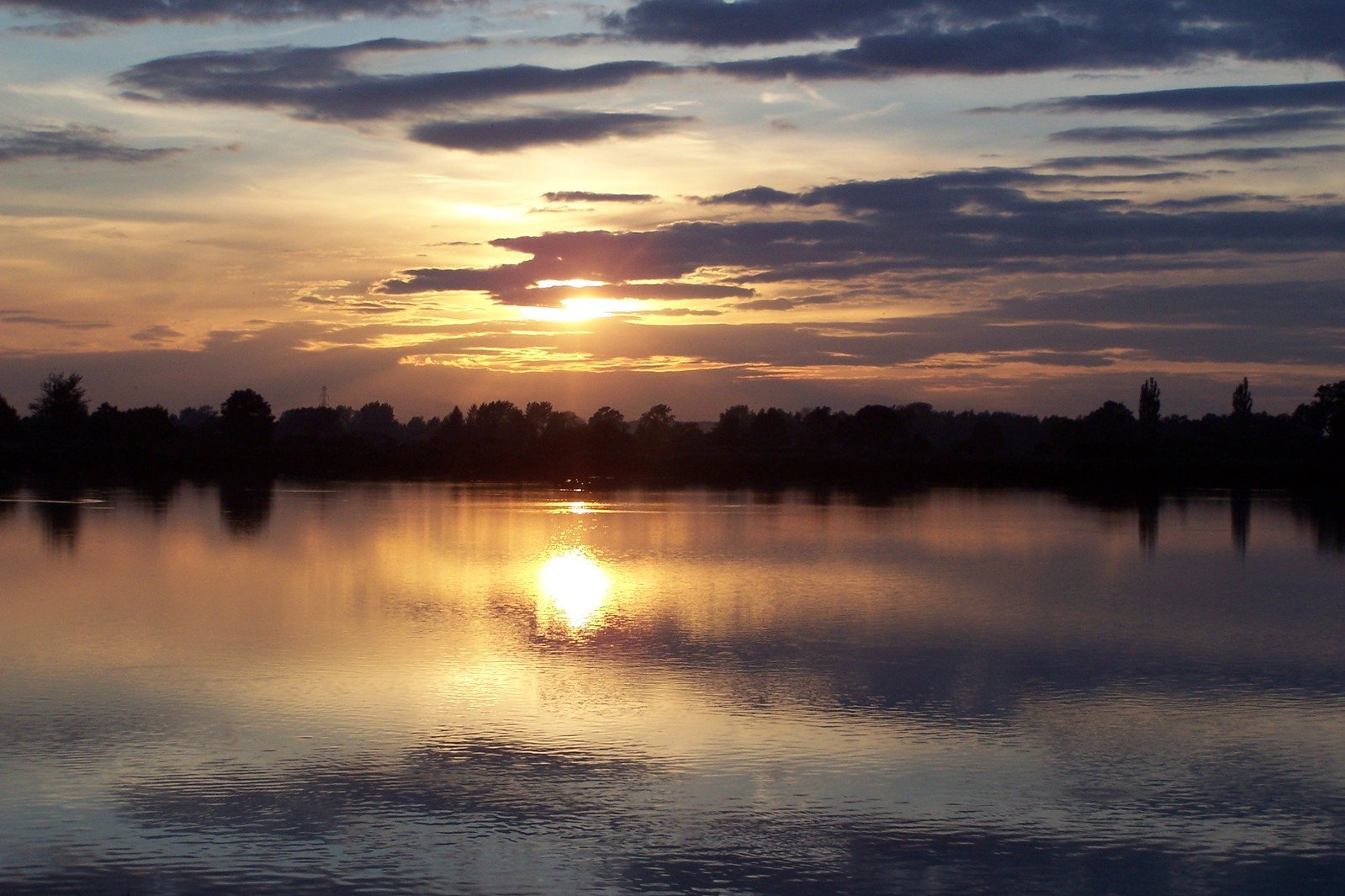 the sun rises over a lake with trees in the background