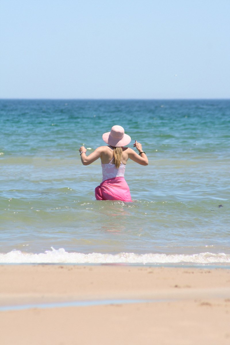 the woman in a pink skirt stands in the ocean