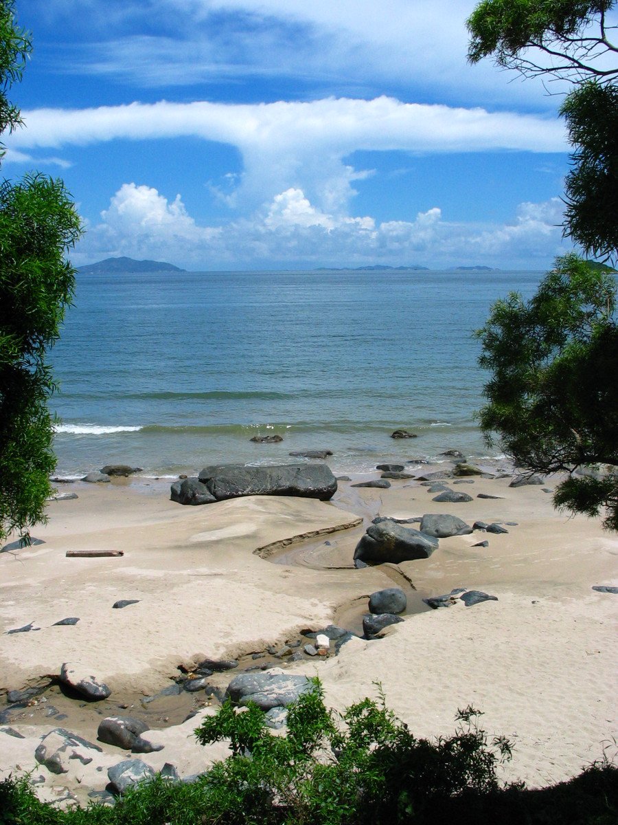 the sea sits next to large rocks that are in the sand