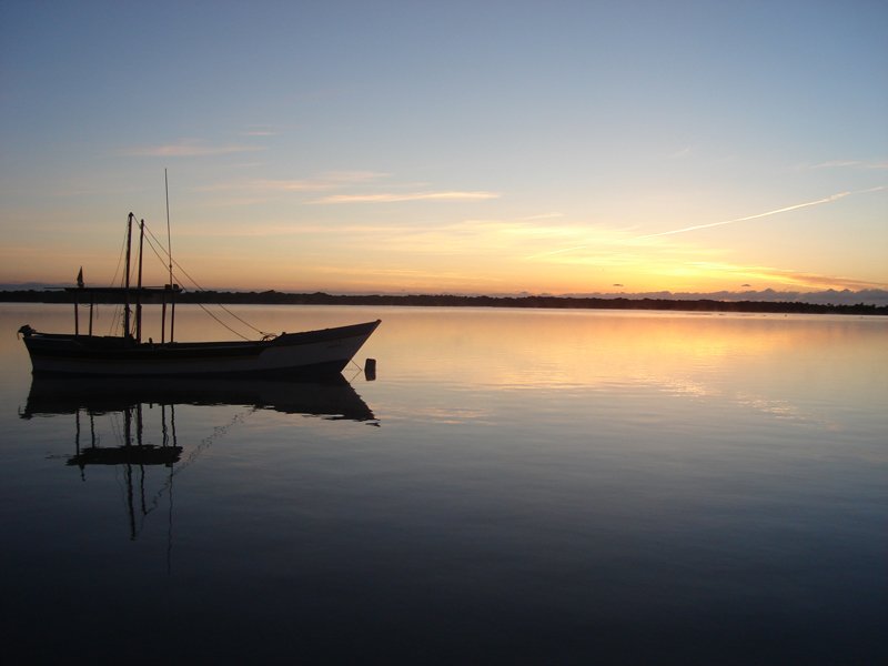a boat in the water with a setting sun behind it