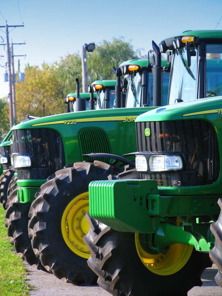 a row of green tractors parked on the side of the road