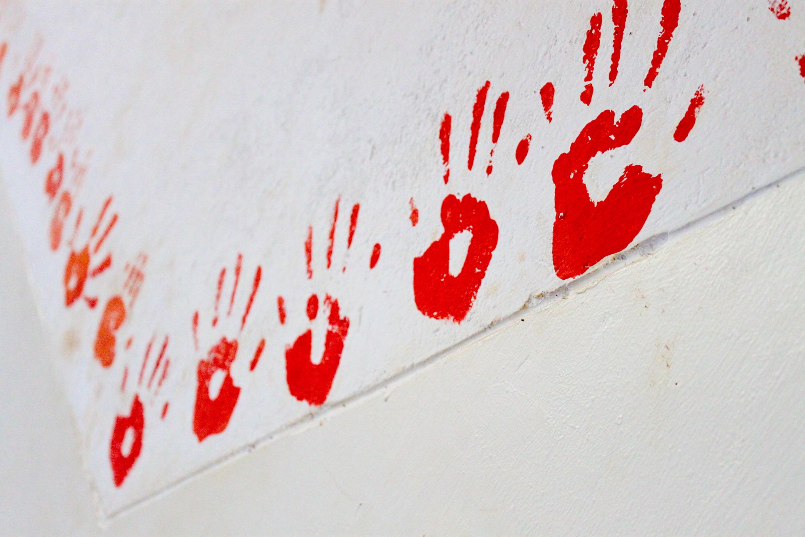 two hands printing red and white paint on a wall