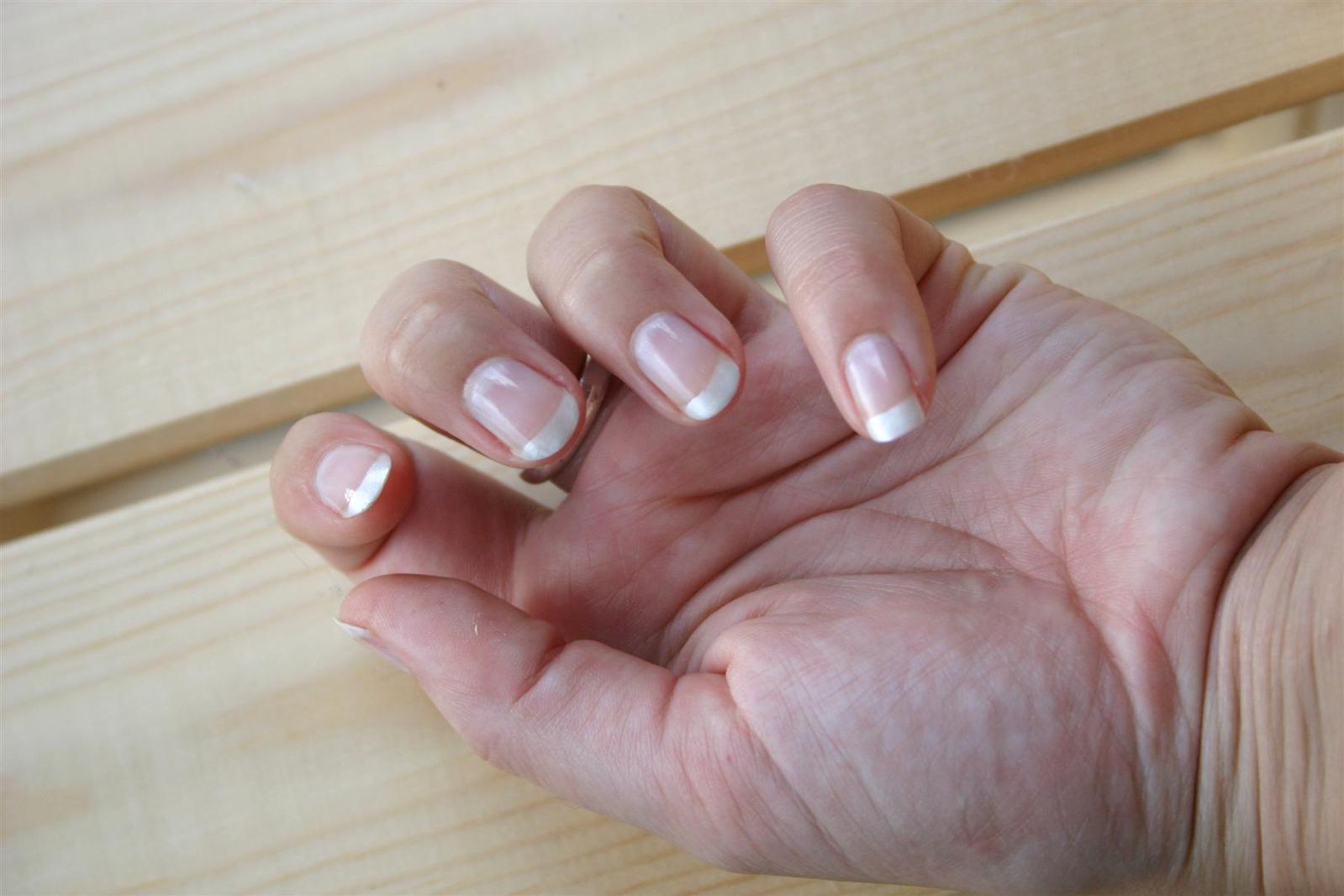 a woman's hands with white nail polish holding her left hand