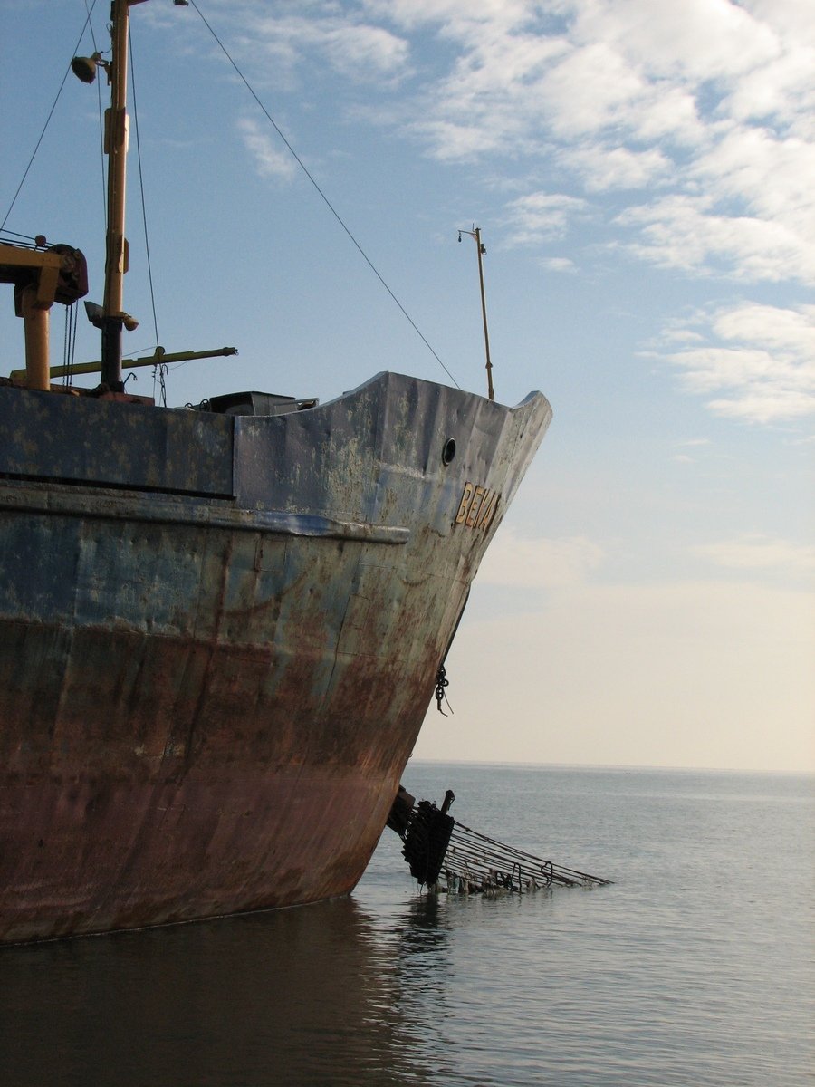a rusted boat in the ocean with a person hanging on it's side