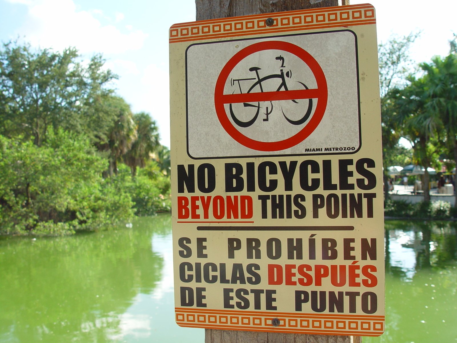 a white sign is posted on a pole near a body of water