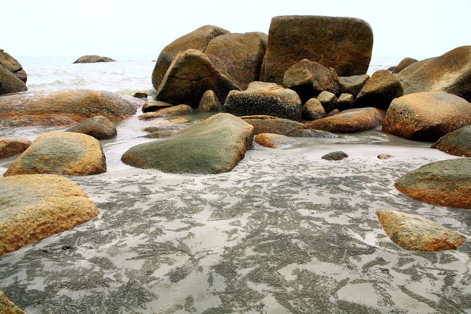 several rocks and sand on the beach next to a body of water