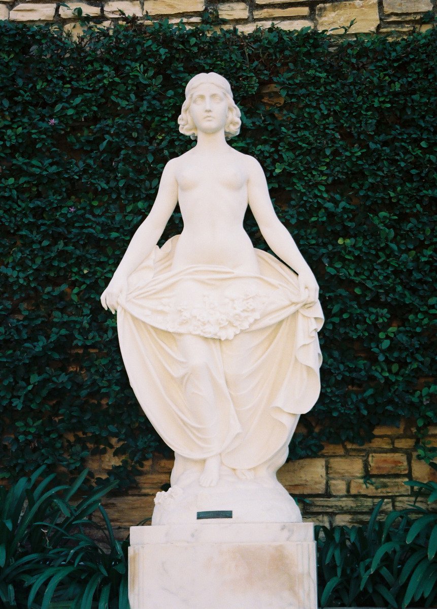 a white statue of a woman in front of plants