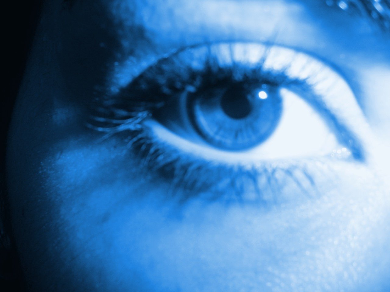 close up of blue woman's eye with water droplets over the left eye