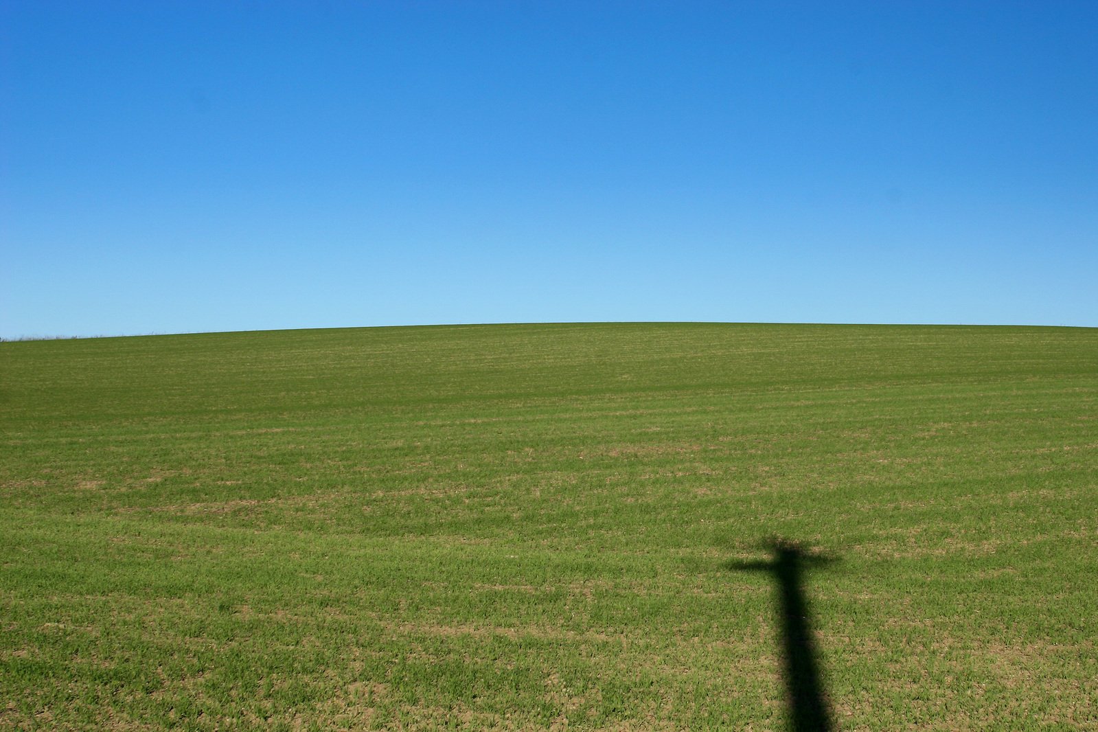 the shadow of a person's head casting a long shadow over an open grass field