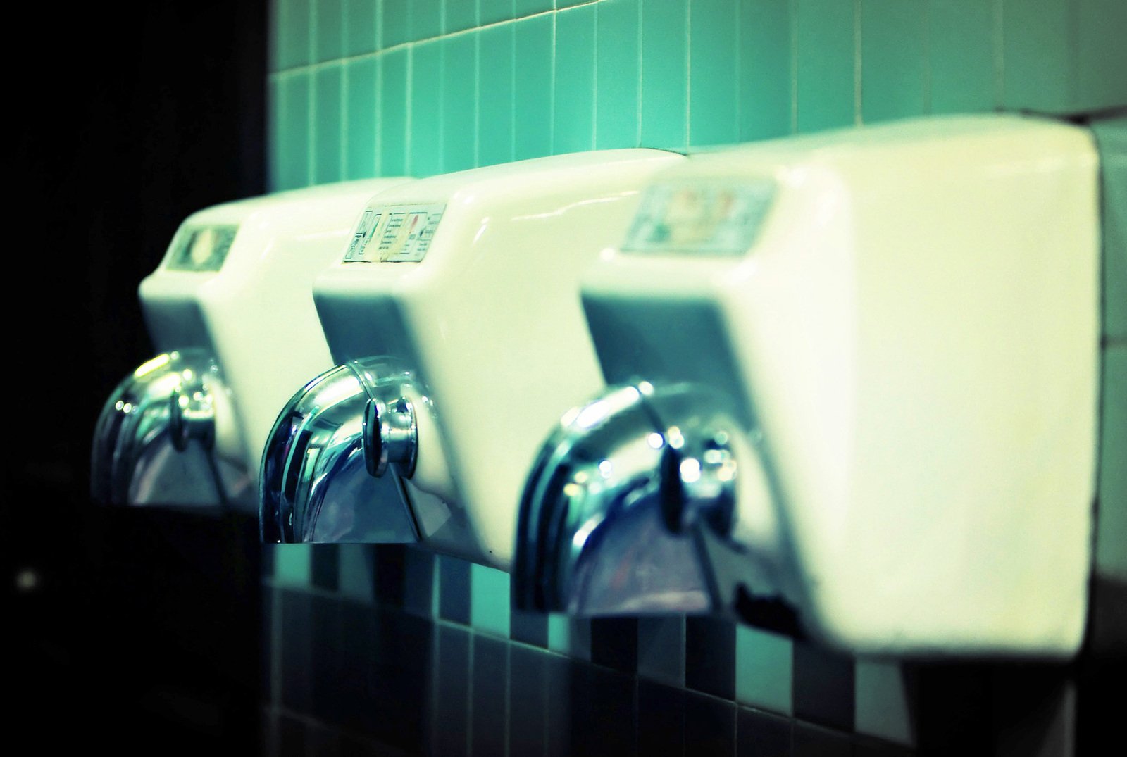 several white urinals on the side of a green wall