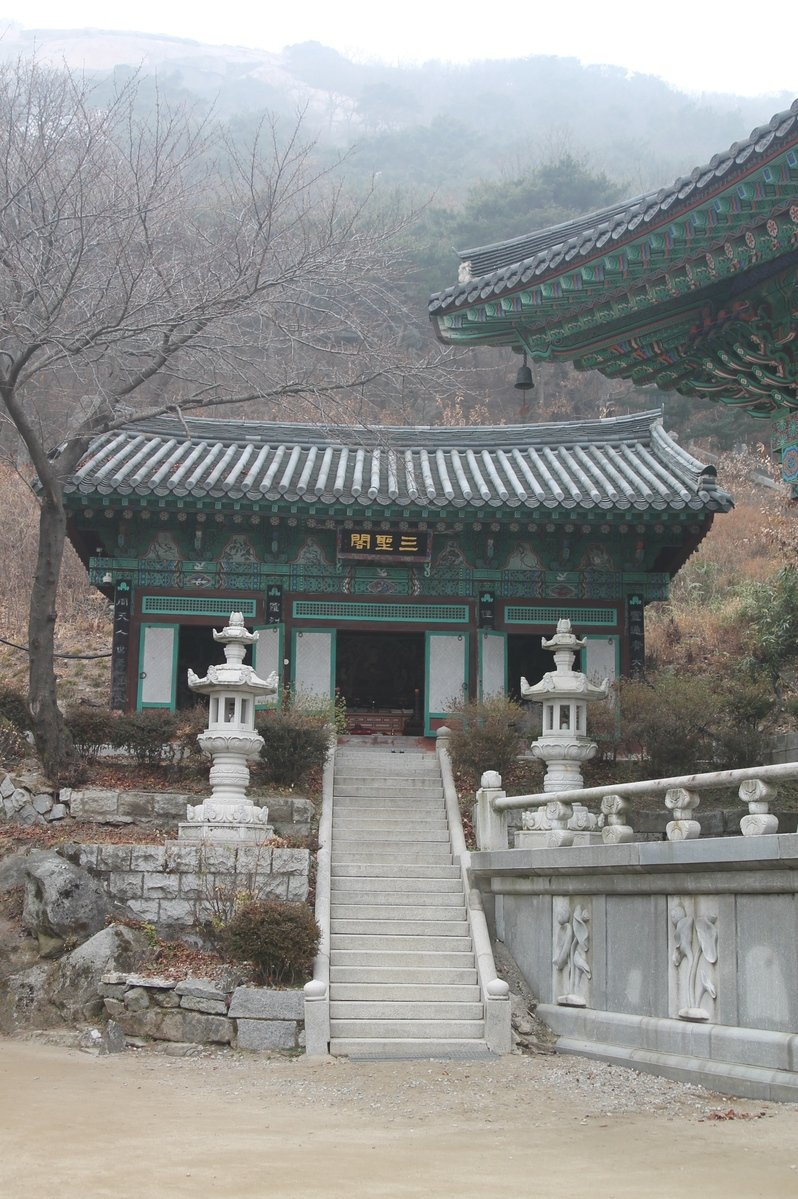 a small pavilion with pillars, two statues and some trees