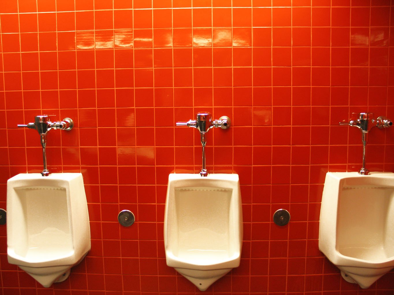 three urinals on red tile wall in men's bathroom