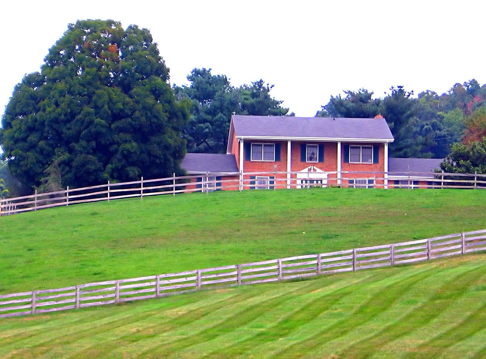 the view of a red brick ranch house in a pasture