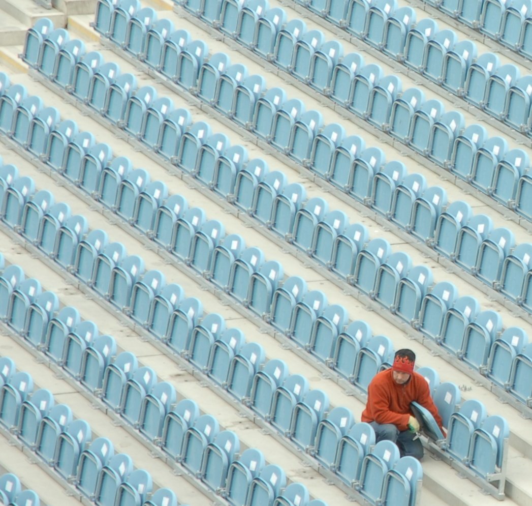 the man is sitting on the bleachers wearing an orange jacket