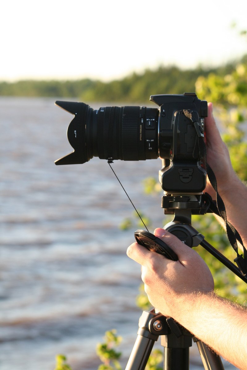 a man holding a camera next to water and holding a remote