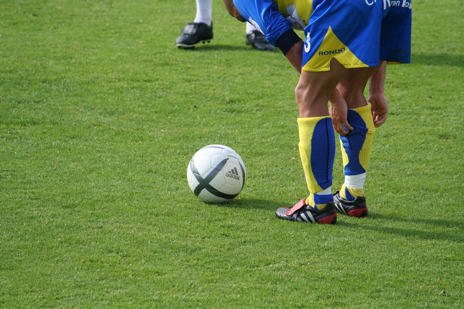 two soccer players from the opposing teams standing near the soccer ball