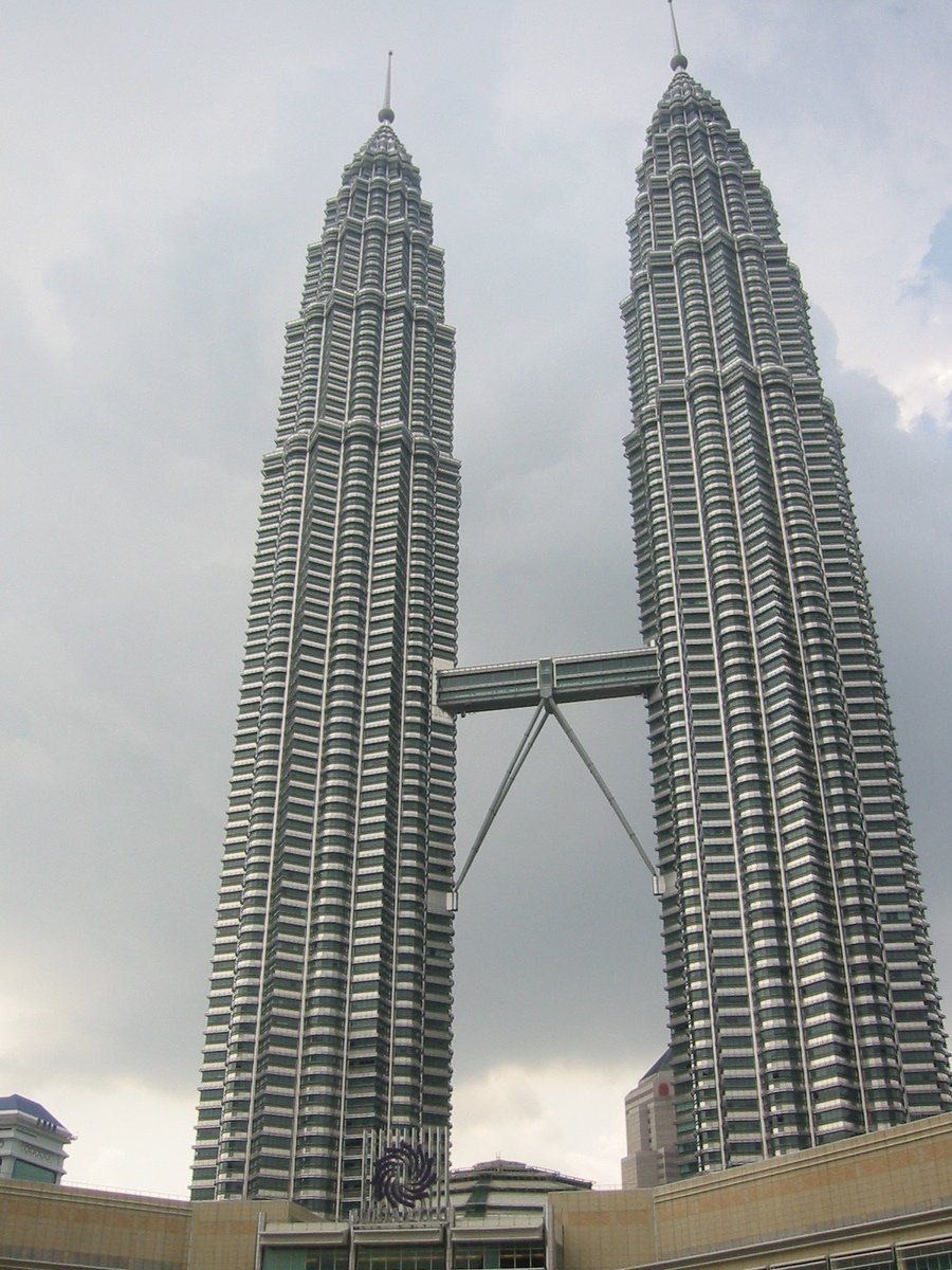 two tall buildings against a cloudy sky in front of other buildings