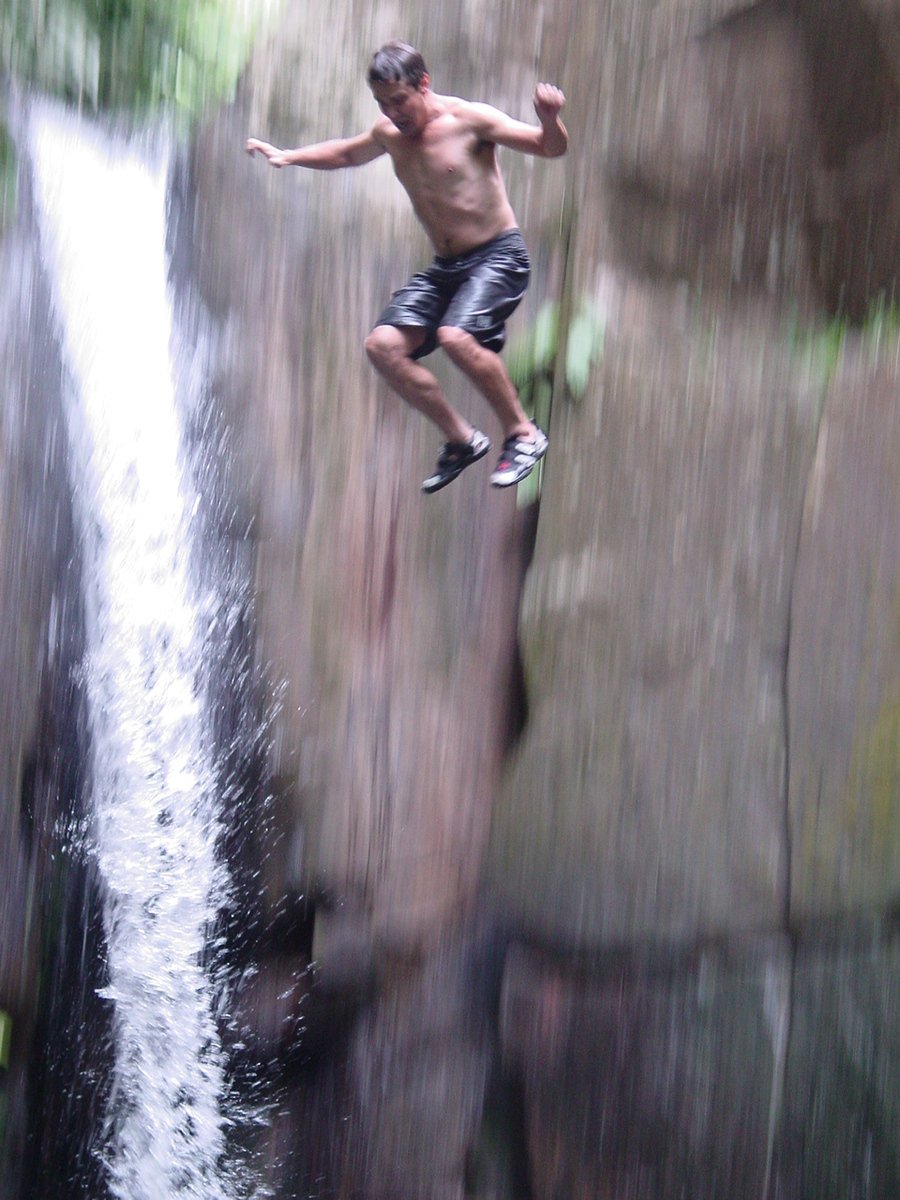 a man standing on a waterfall with  on and his shirt off while holding his hands up