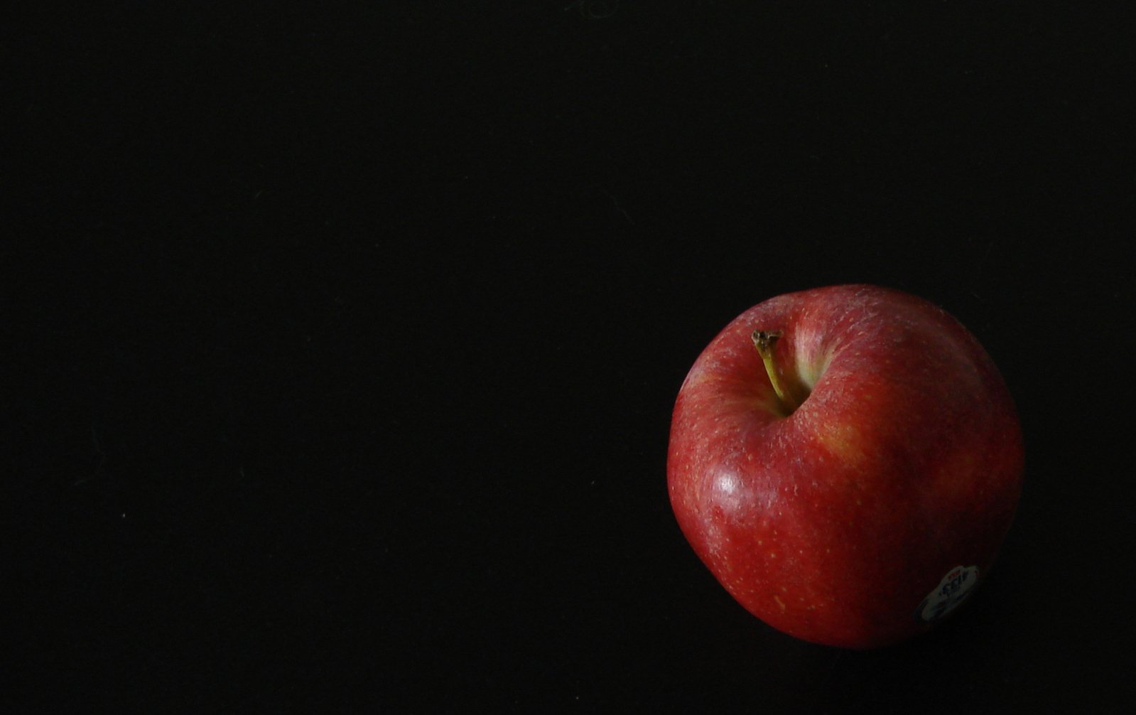 a single apple on a black surface with lighting