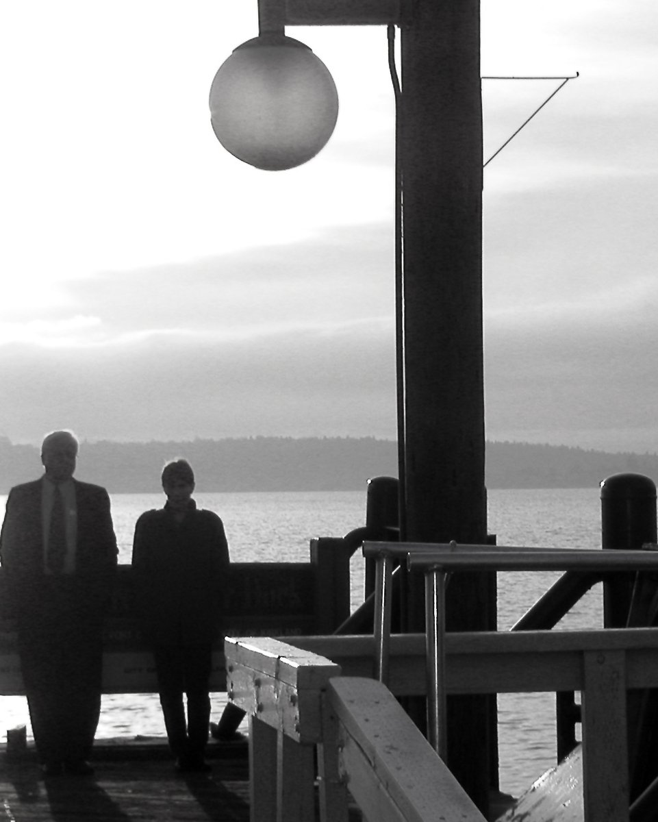 two men sitting on a bench on a pier