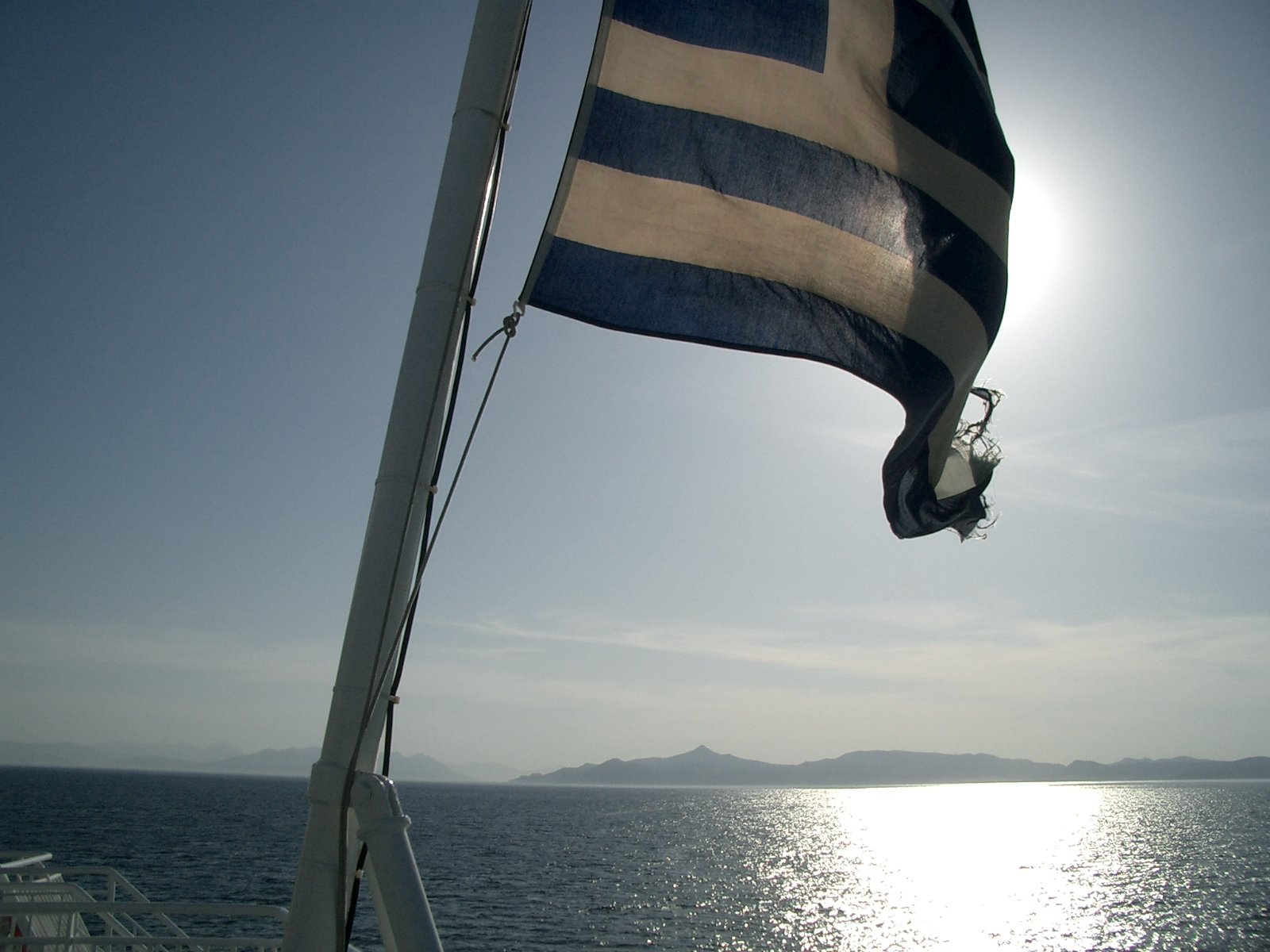 a greek flag flies next to the ocean on a boat