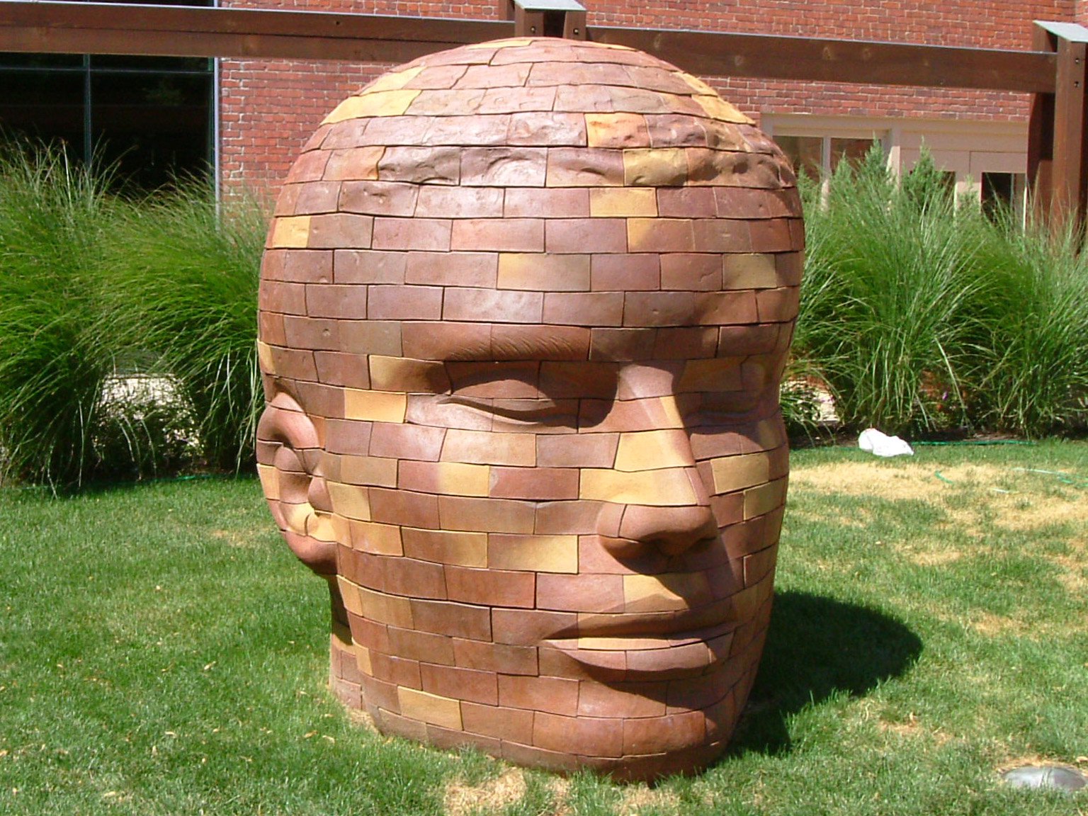 a large brick sculpture is in the grass near a brick building
