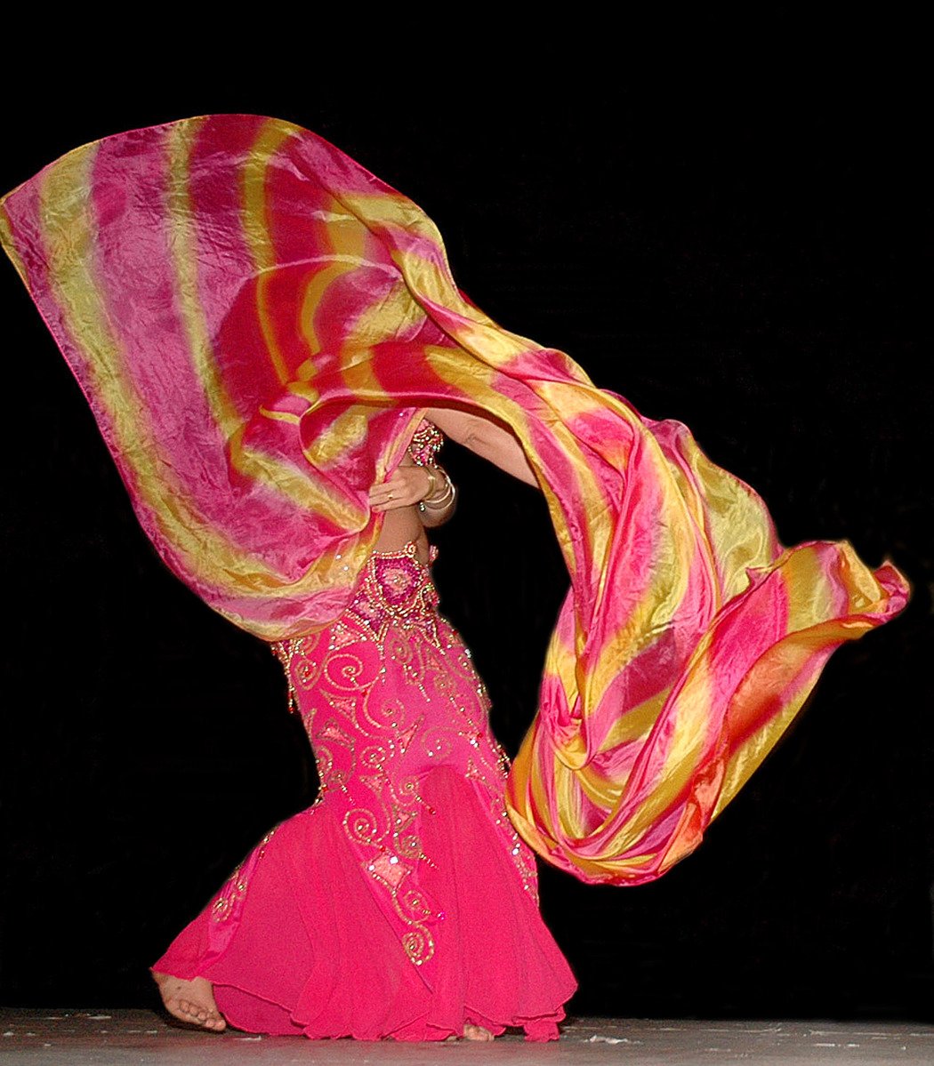 a woman in a pink dress dances with a long scarf