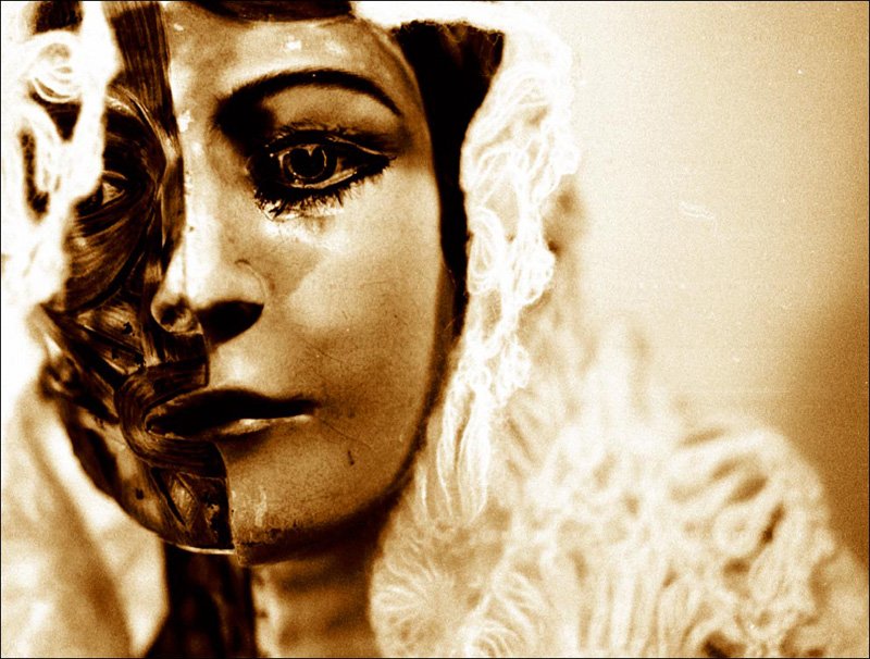 a sepia - toned pograph of a woman with a large nose and face painted with black, gold and white feathers