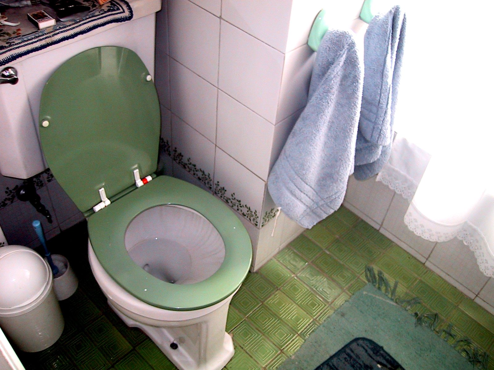 an empty bathroom with a green toilet and blue towels
