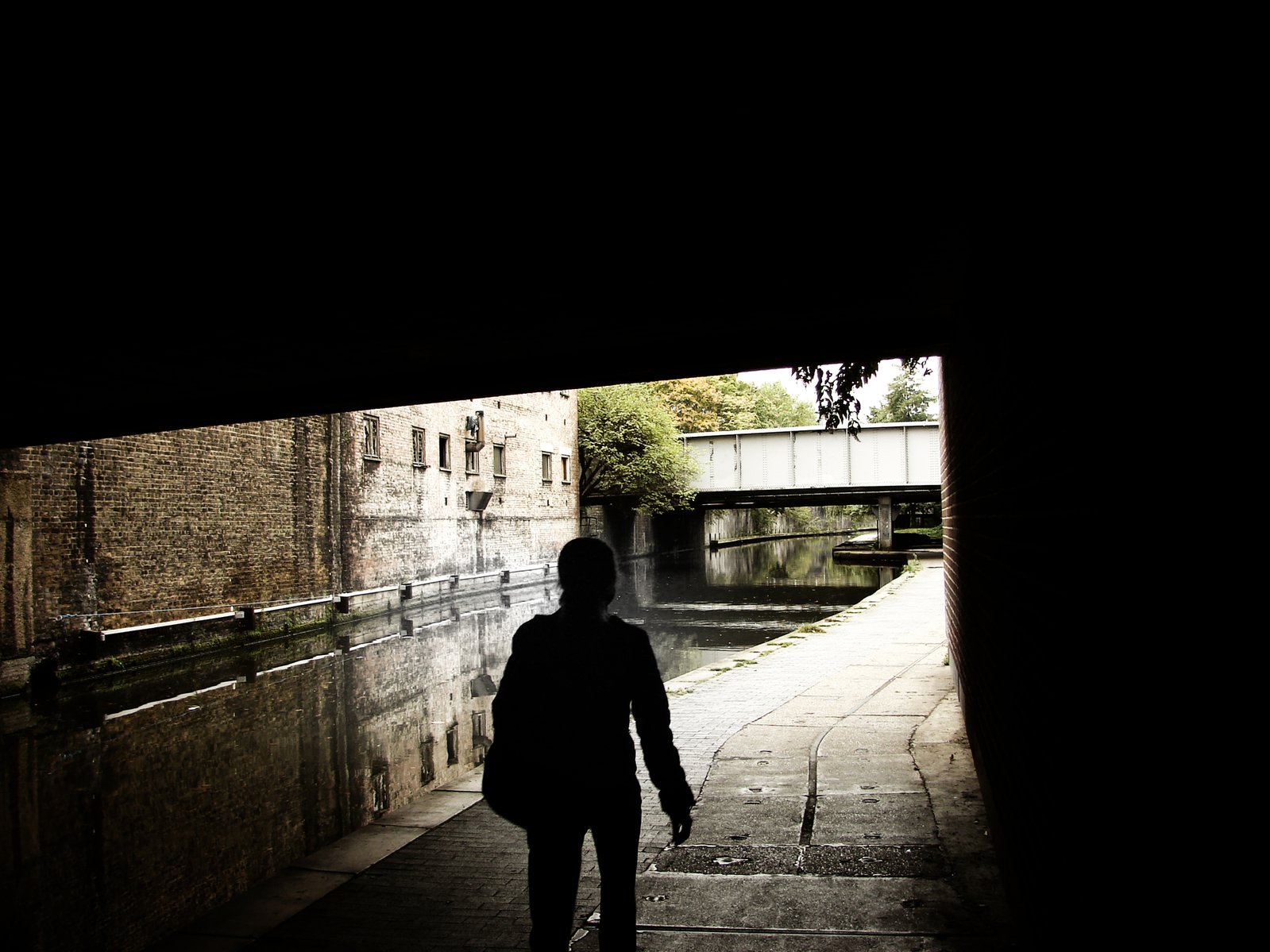 person walks under a tunnel at dusk on an unpaved walkway
